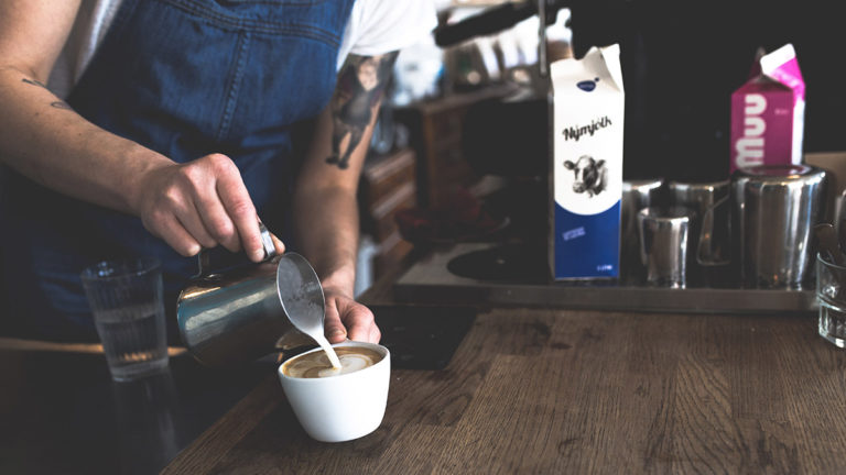 Milch wird in eine Kaffeetasse gegossen