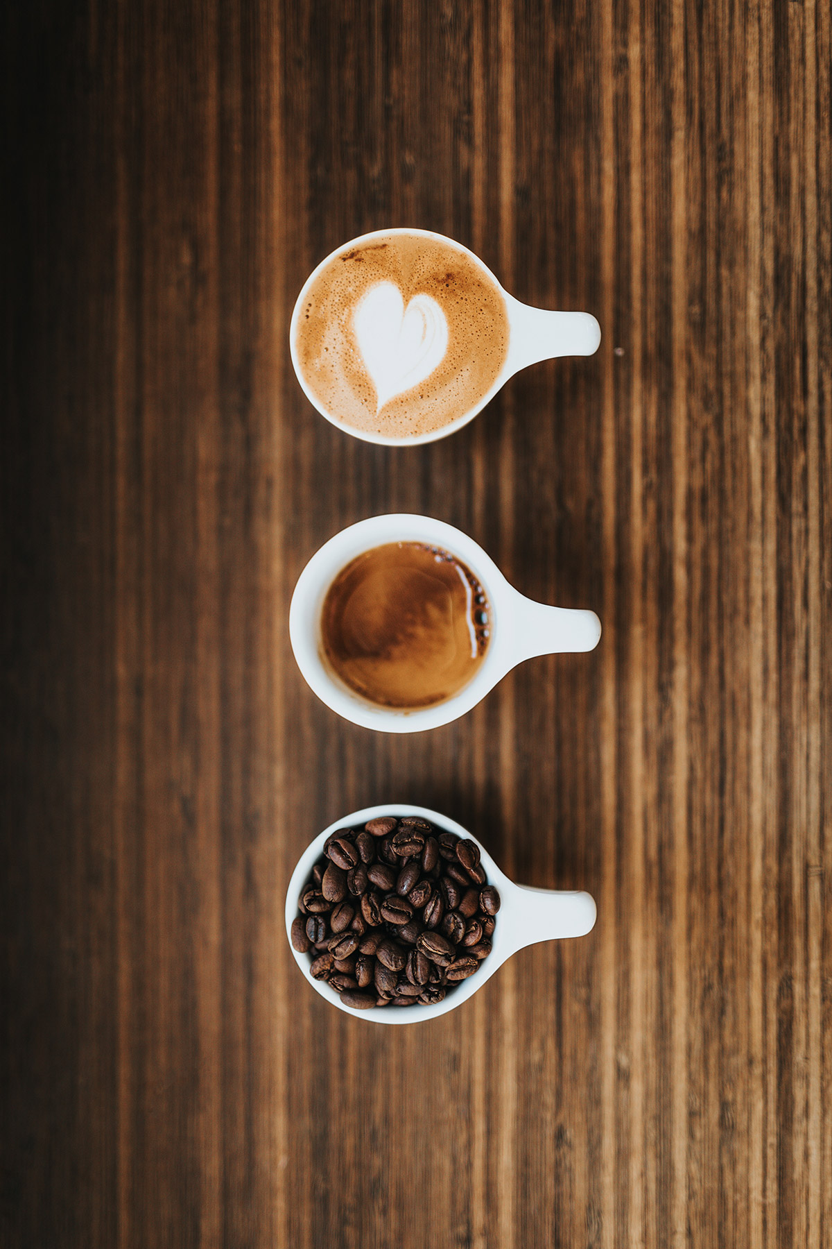 Cappuccino mit Latte Art, Espresso und Kaffeebohnen in einer Reihe