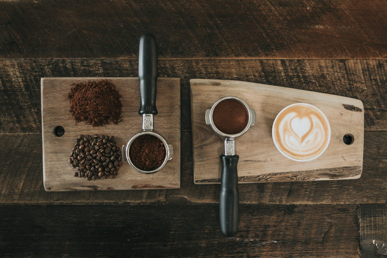 Siebträger mit Kaffeemehl und Cappuccino auf einem Holzbrett